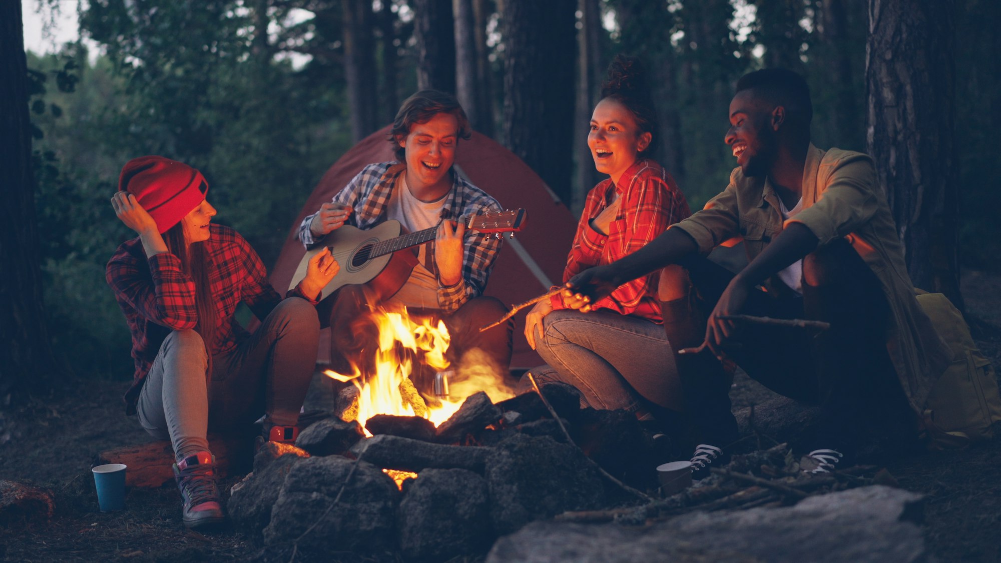 Friends laughing around a campfire in the woods at the end of the season